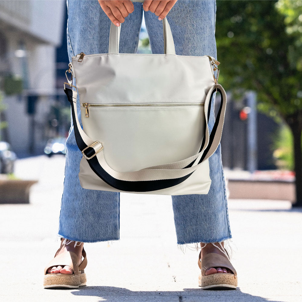 Person holding the Cream Jill Tote with black/Cream strap on a city street.