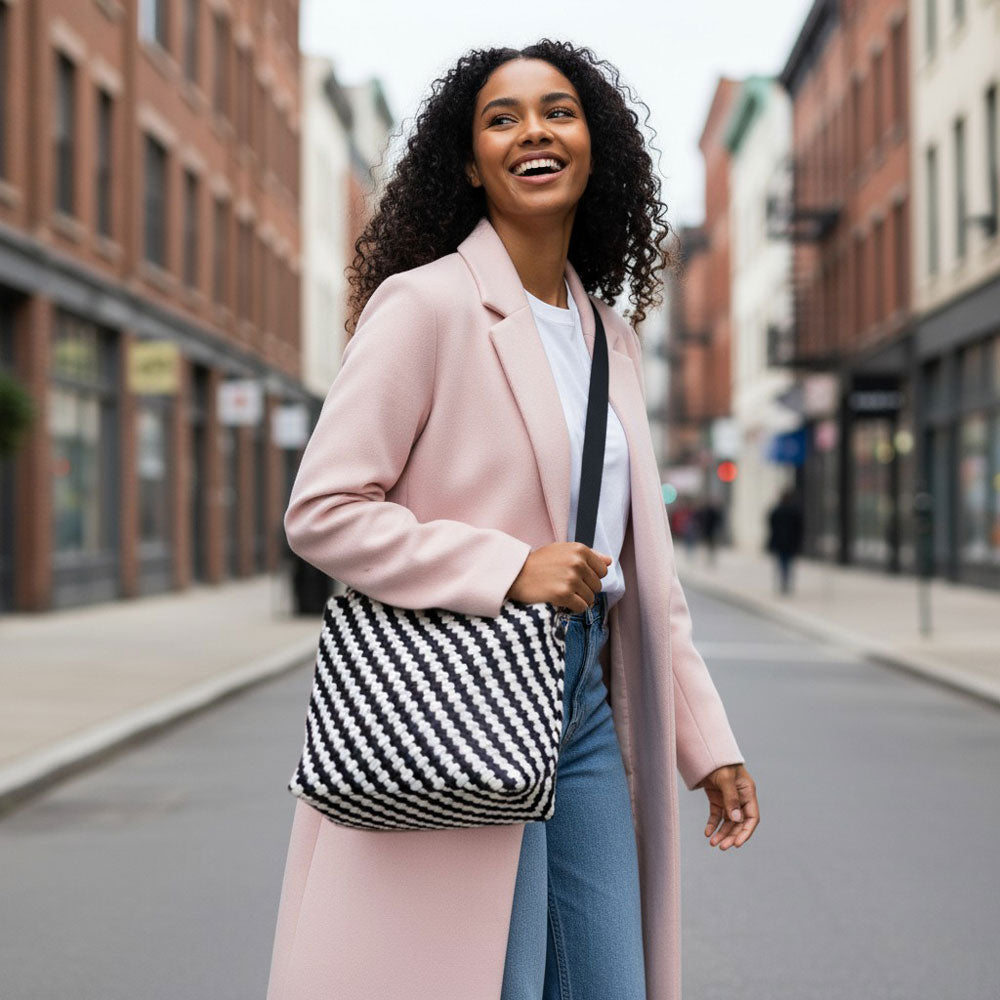 Woman in a pink coat with a black and white striped tote on a city street