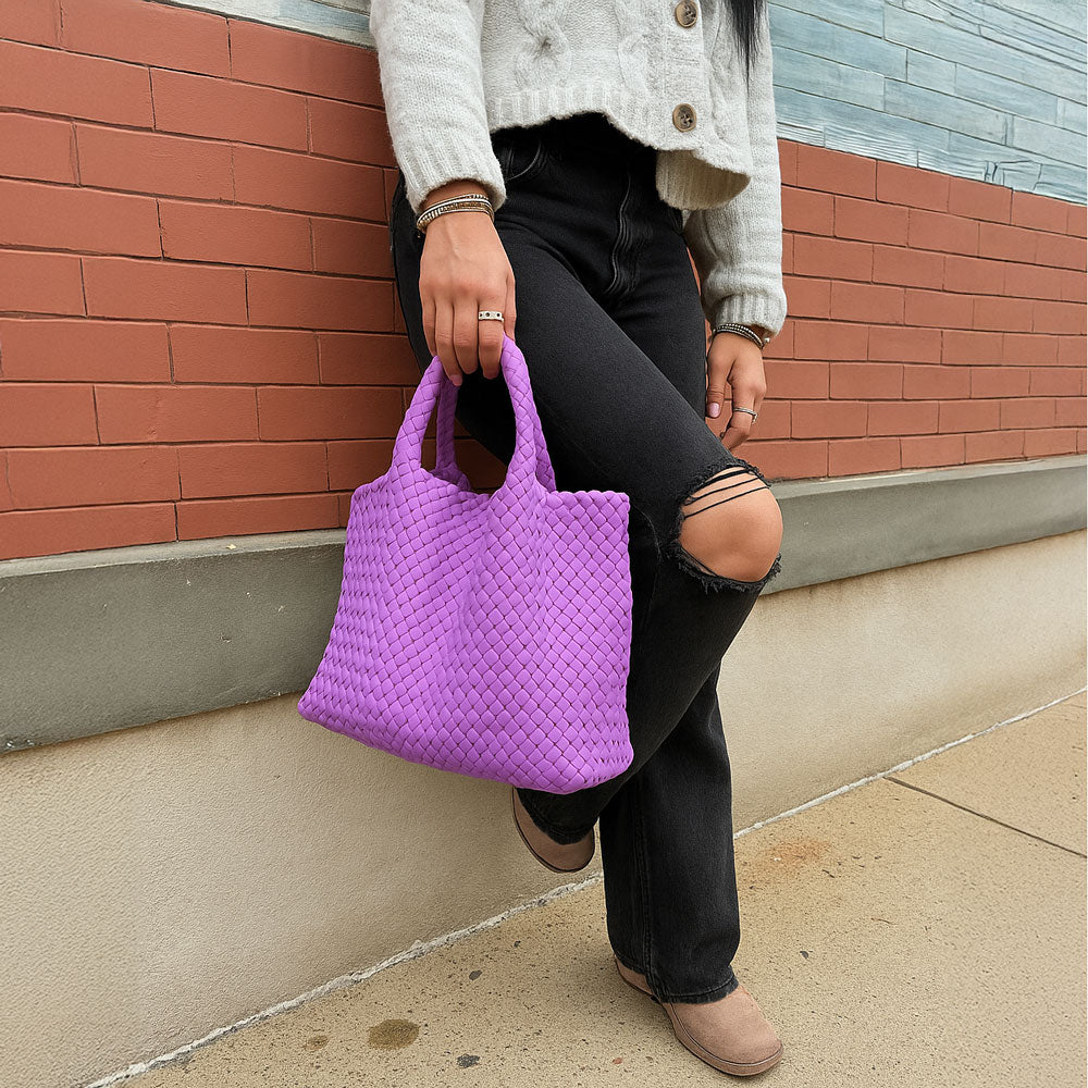 Person holding a lilac woven tote against a brick wall.