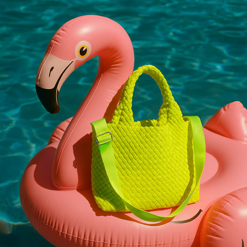Pink inflatable flamingo with a neon yellow woven neoprene tote on a blue water background