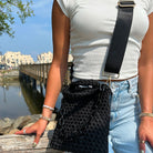 Woman wearing the Lola handbag as a crossbody bag, sitting outside