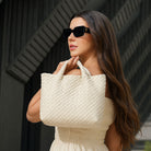 Woman holding a white quilted handbag with sunglasses on a blurred background