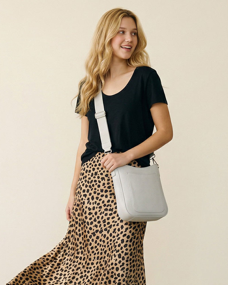Woman wearing a cream crossbody bag wearing a black top and leopard print skirt on a beige background