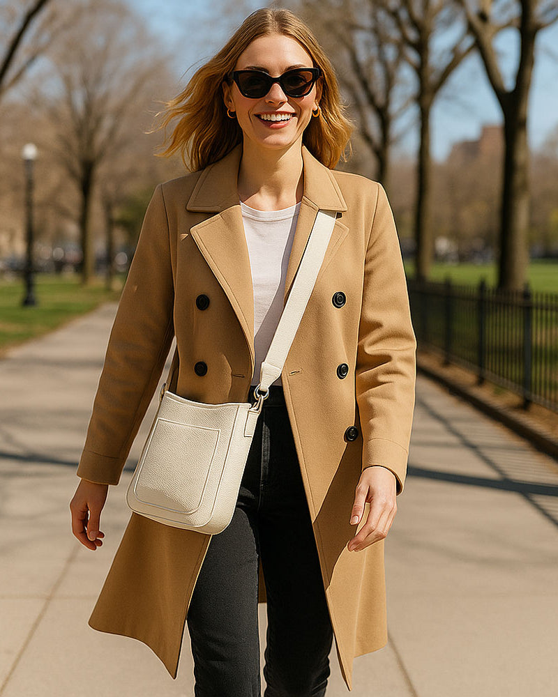 Woman in a tan coat walking on a sidewalk in a park-like setting