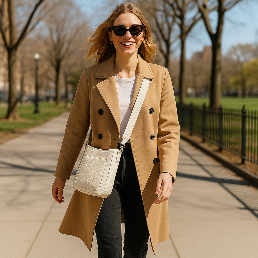Woman in a tan coat walking on a sidewalk in a park-like setting