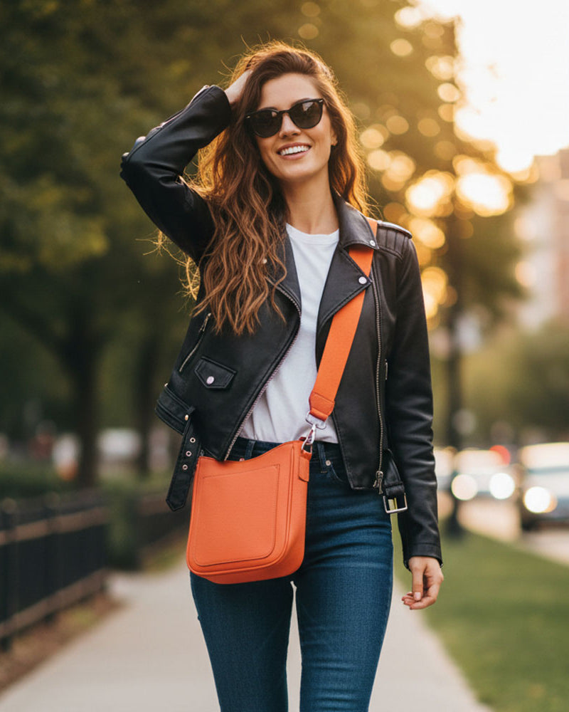 Woman with an orange bag walking on a sidewalk with a blurred city background.
