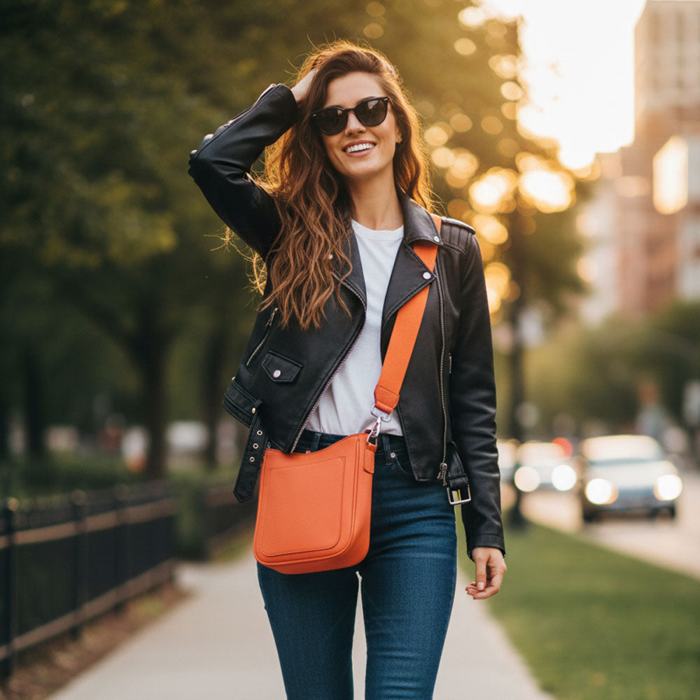 Woman with an orange bag walking on a sidewalk with a blurred city background.
