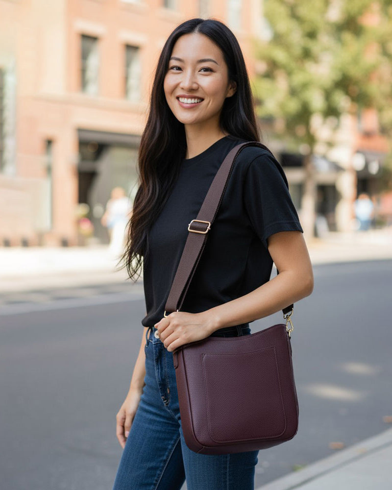 Woman holding a maroon crossbody bag on a city street