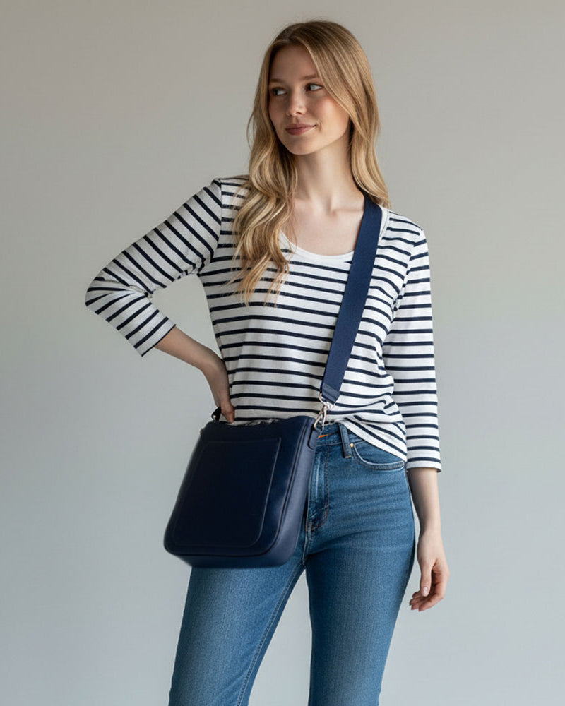 Woman wearing a striped shirt and jeans with a navy bag on a plain background