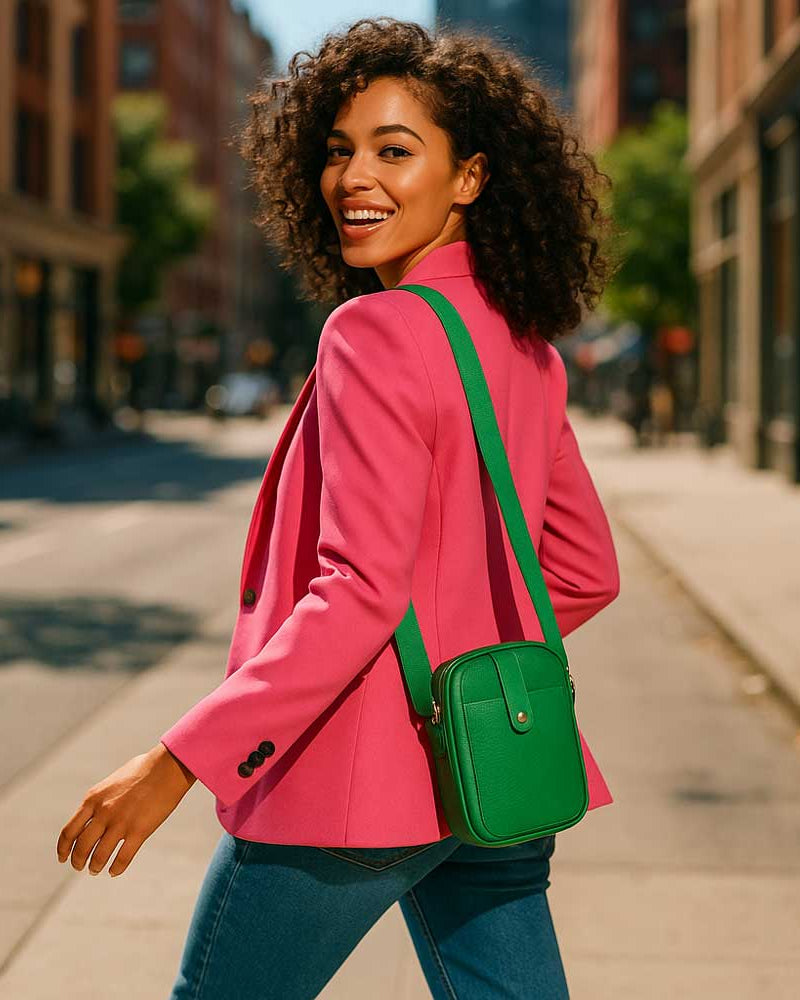 Woman in a pink blazer with a green bag walking on a city street.