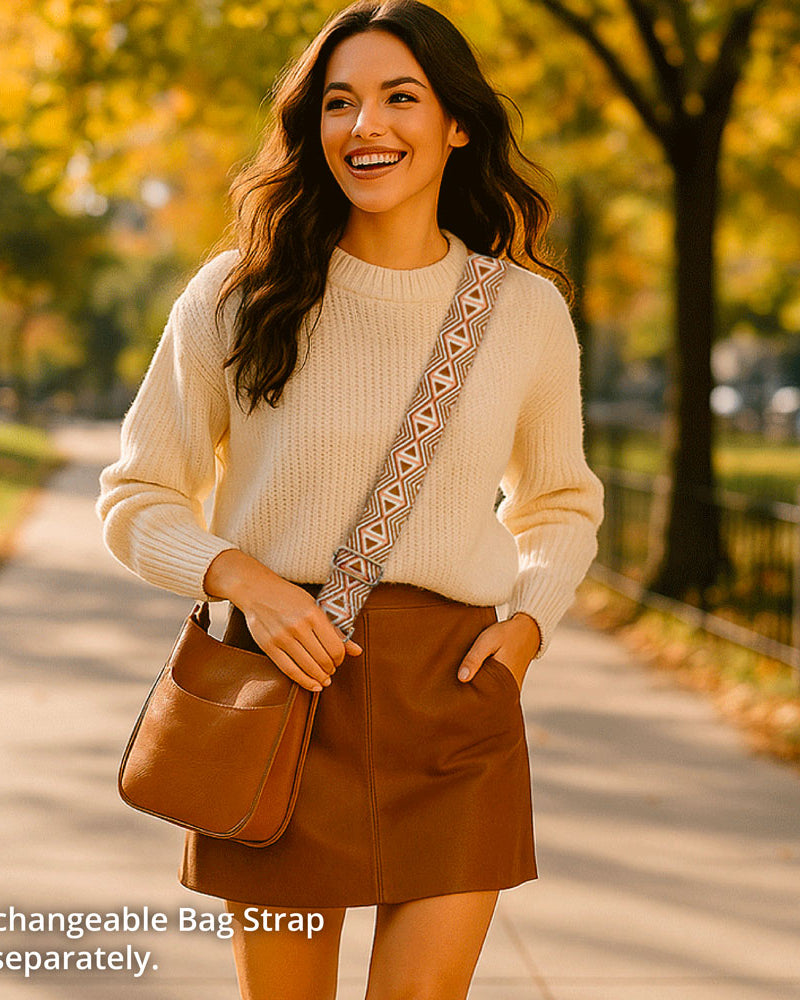 Woman walking outdoors in a park with a camel vegan leather bag and beige sweater.