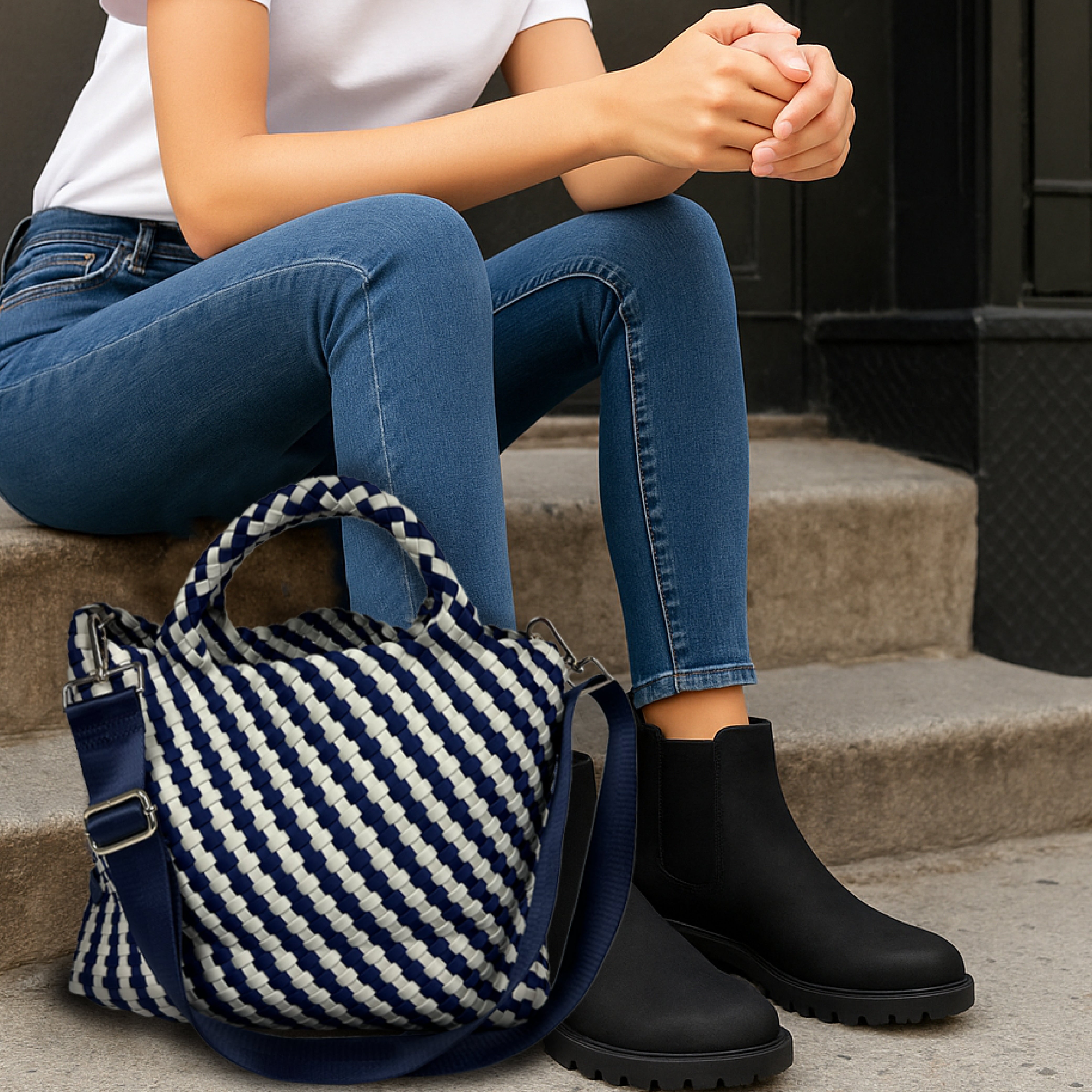 Woman in denim and a white tee sitting on steps with a navy/ecru striped lily tote by her feet.