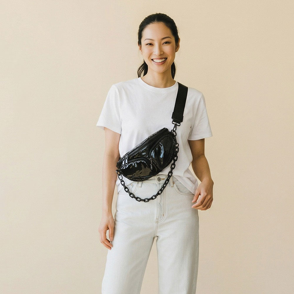 Woman wearing a black liquid nylon sling bag on a beige background