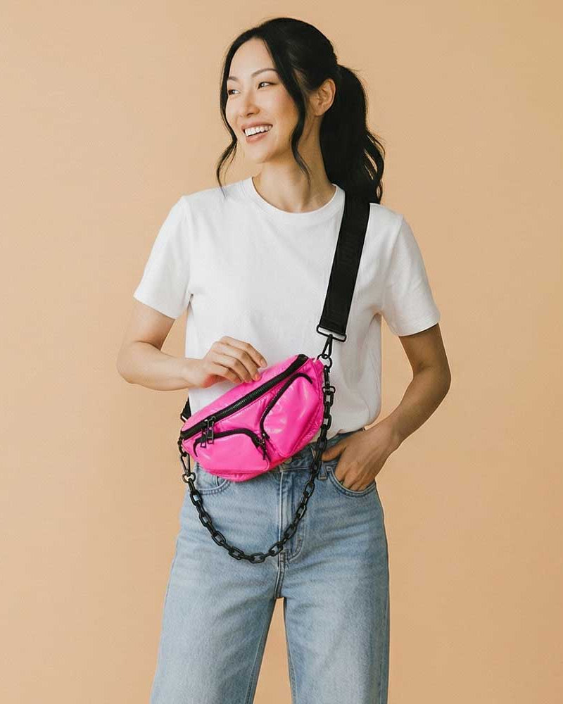 Woman wearing a pink sling bag with a black chain on a beige background