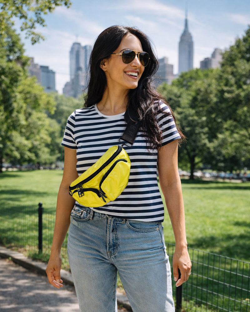 Woman in a striped shirt and sunglasses with a yellow bag in a park with city skyline in the background
