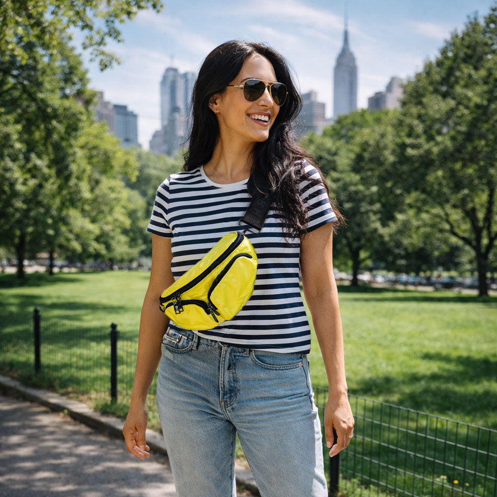 Woman in a striped shirt and sunglasses with a yellow bag in a park with city skyline in the background