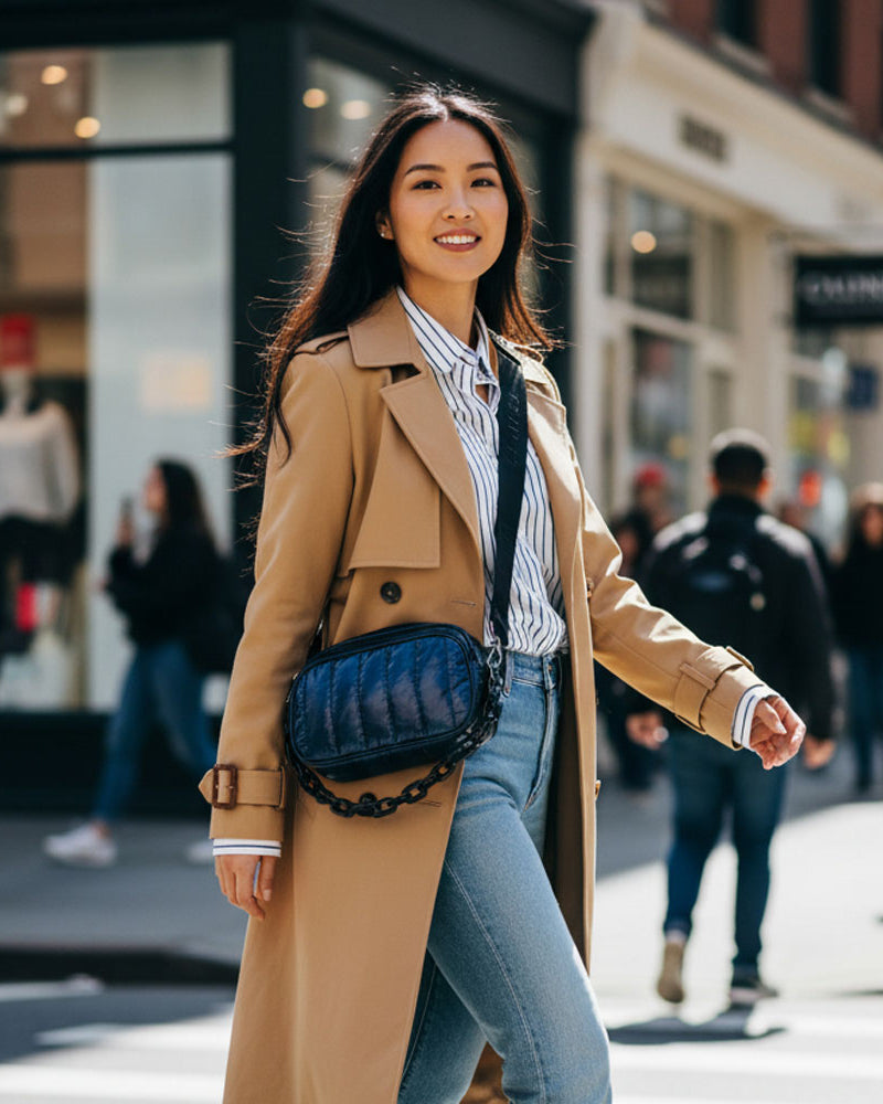 Woman in a tan coat with a navy handbag walking on a city street.