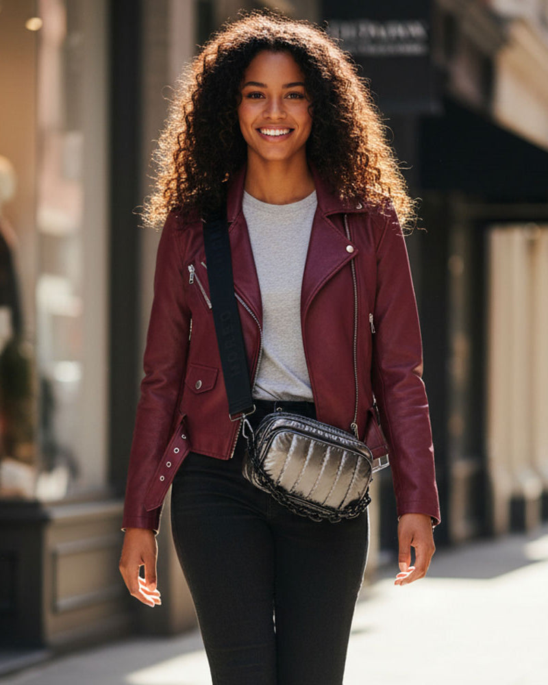 Woman wearing a maroon leather jacket and black pants on a city street. Wearing a pewter crossbody bag.