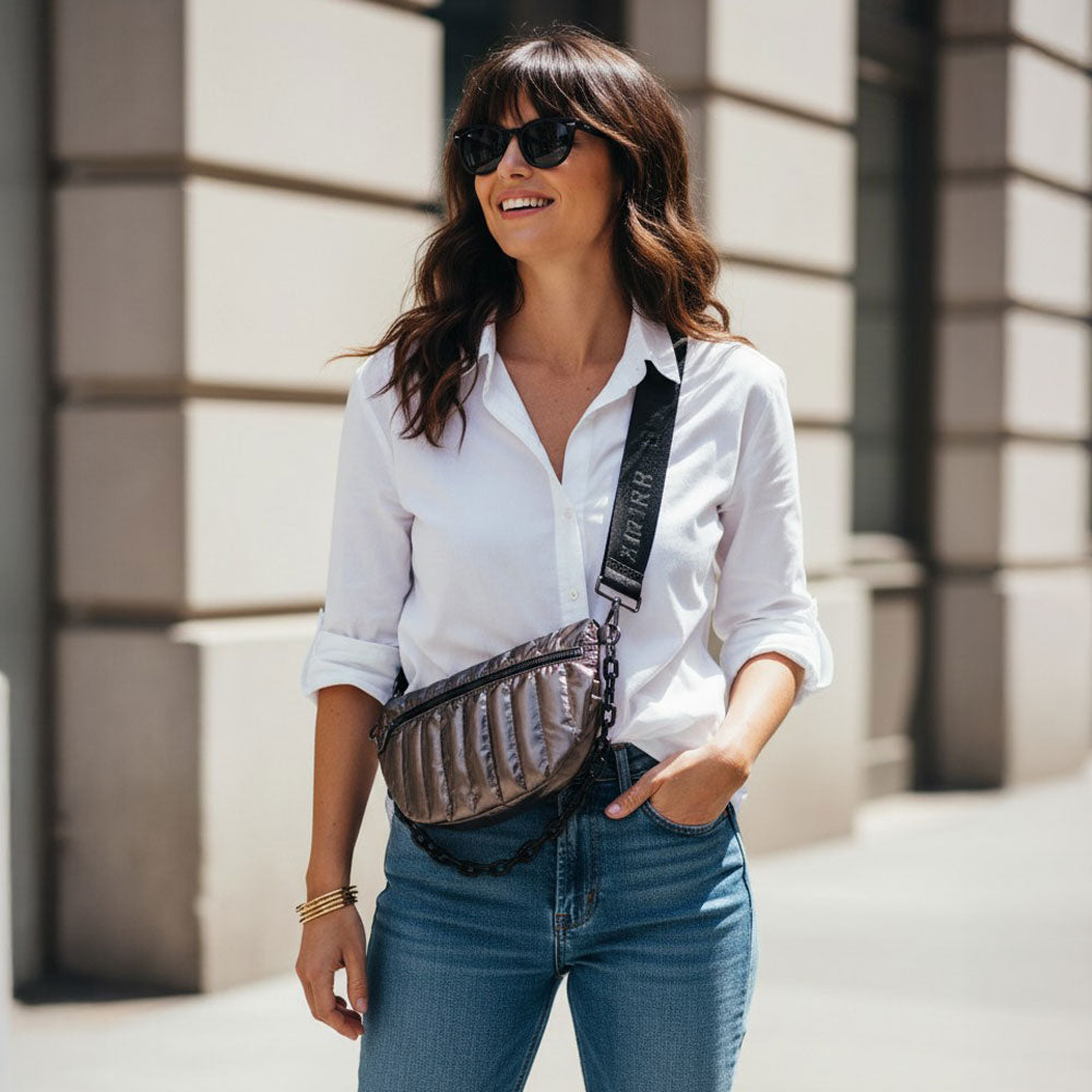 Woman wearing a white shirt, blue jeans, and sunglasses with a bronze crossbody bag.