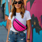 Woman wearing a white t-shirt, blue jeans, and the Reese Sling in Pink with a colorful mural background