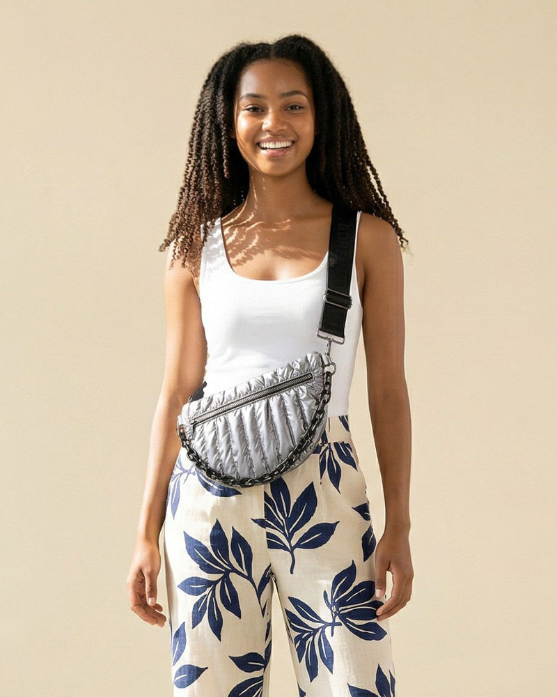 Woman wearing a sliver quilted nylon sling bag against a beige background