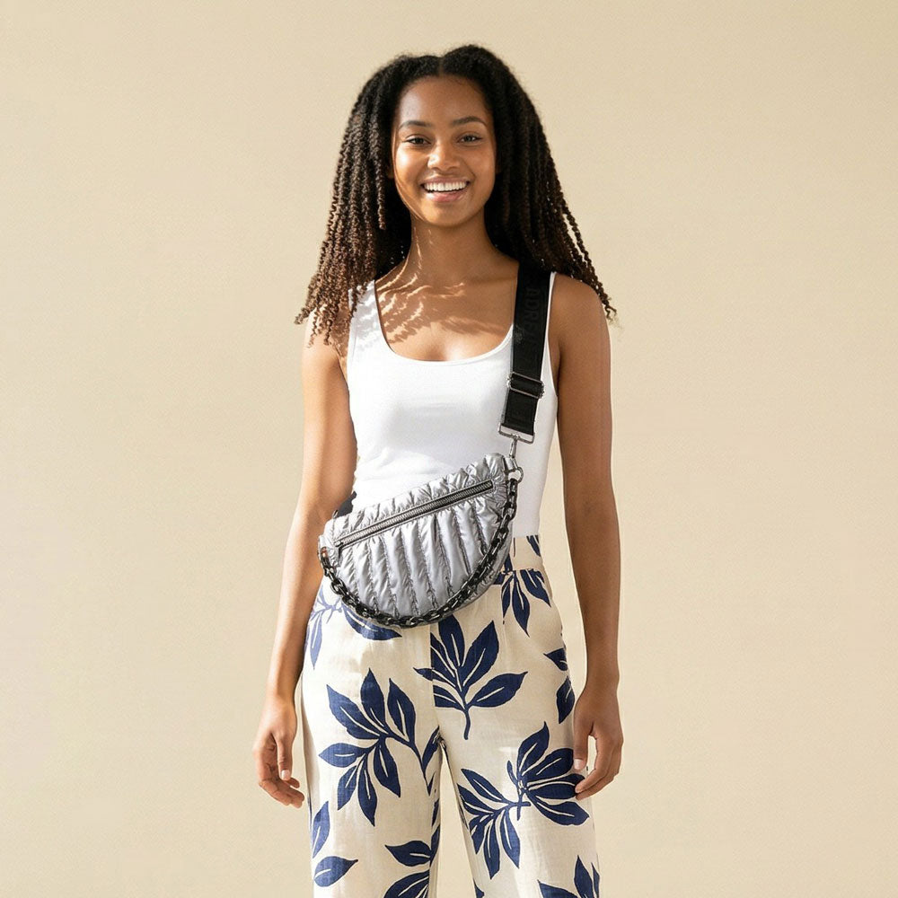 Woman wearing a sliver quilted nylon sling bag against a beige background