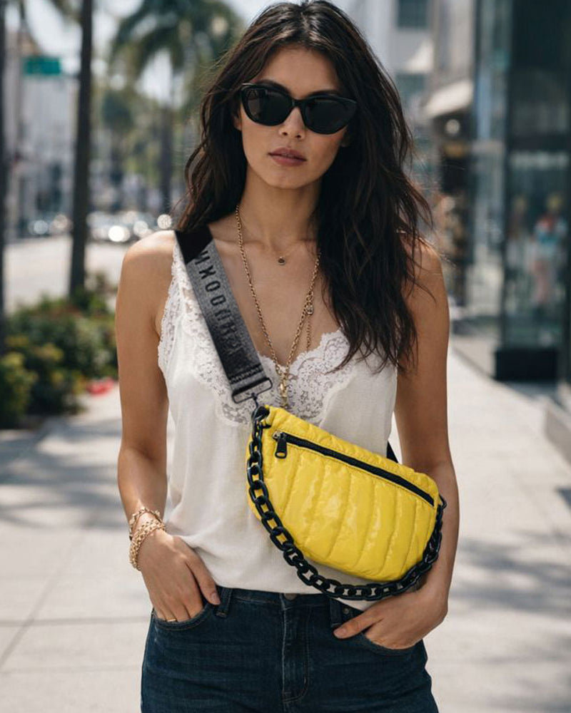 Woman walking on a sidewalk wearing a yellow quilted bag and sunglasses.
