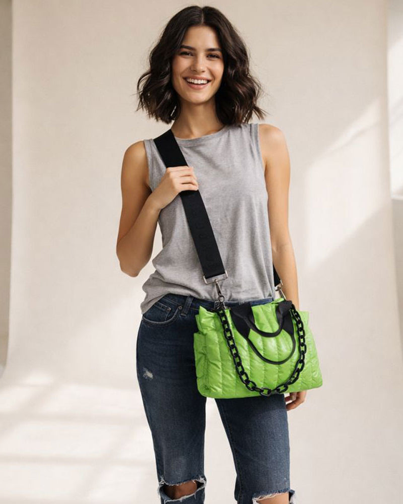 Woman holding a green quilted nylon tote with a black strap against a neutral background