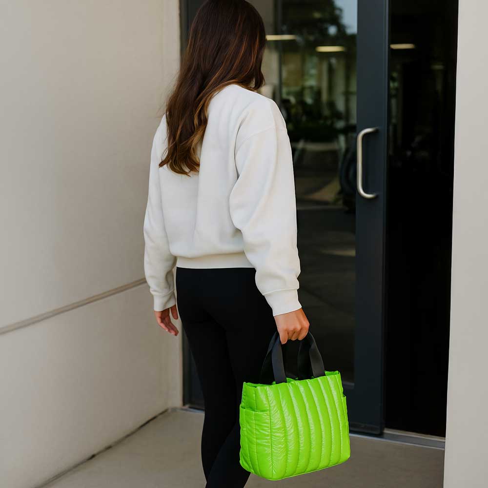 Person holding a bright green tote in front of a building entrance