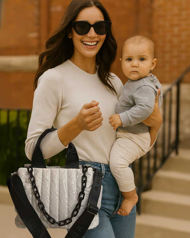 Woman holding a baby and smiling outdoors. Holding a white tote