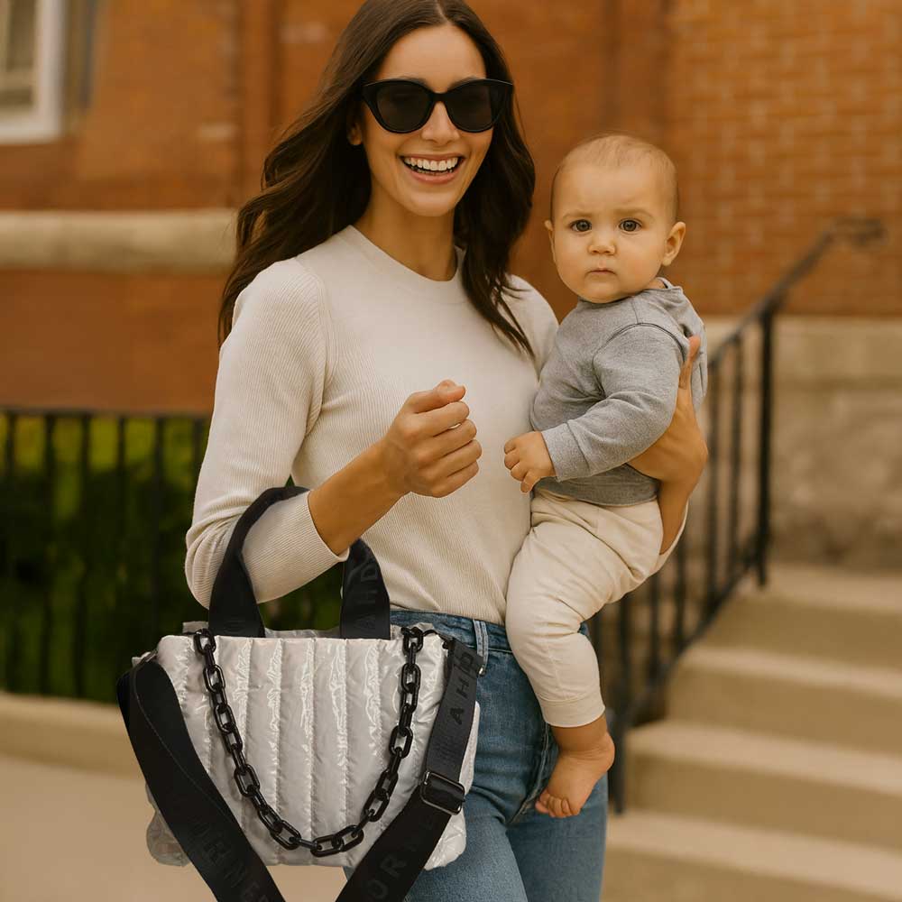 Woman holding a baby and smiling outdoors. Holding a white tote