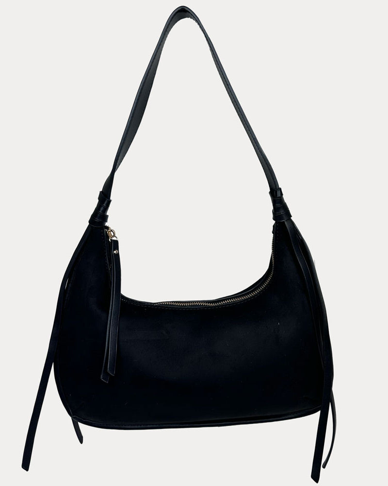 A black vegan suede shoulder bag with a vegan leather details, shown against a light gray