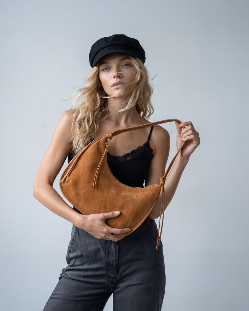 Woman holding a vegan suede shoulder bag with vegan leather details in camel. Set on a light grey background