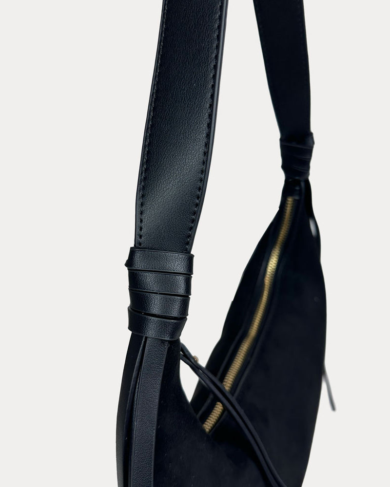 Close-up of a black vegan leather shoulder bag, showing the strap detail against a light gray background.
