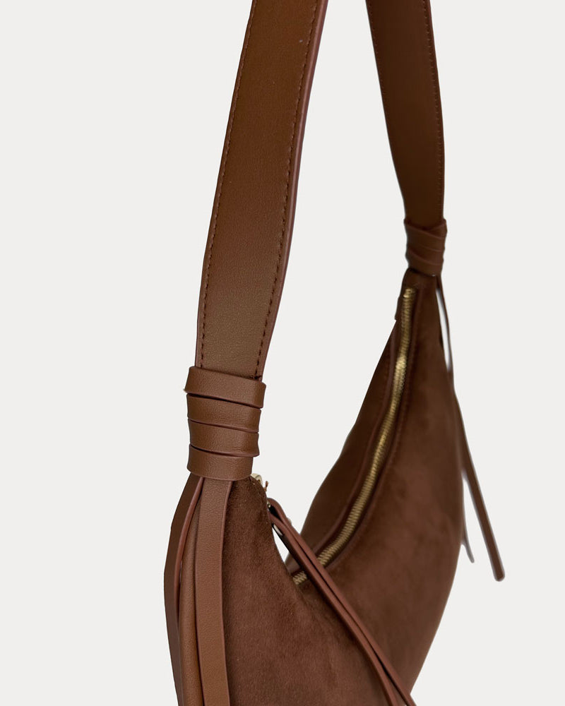 A close-up side view of a chocolate vegan suede with vegan leather details shoulder bag, set against a plain light gray background.