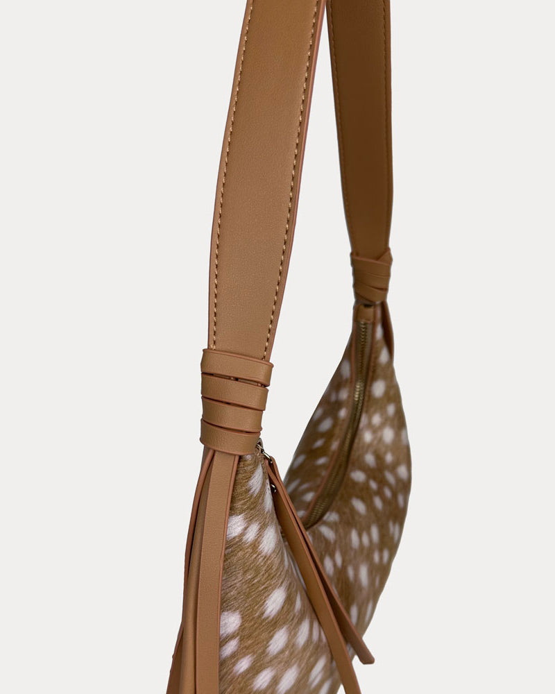 Close-up of a shoulder bag with camel vegan leather strap and deer print body, shown against a light gray background.