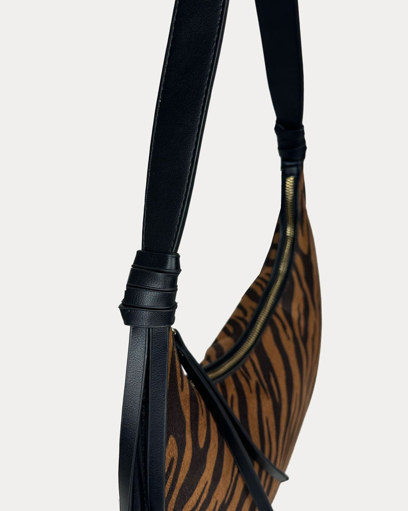 A close-up of a shoulder bag featuring a brown and black tiger-stripe patterned body with a black vegan leather strap.