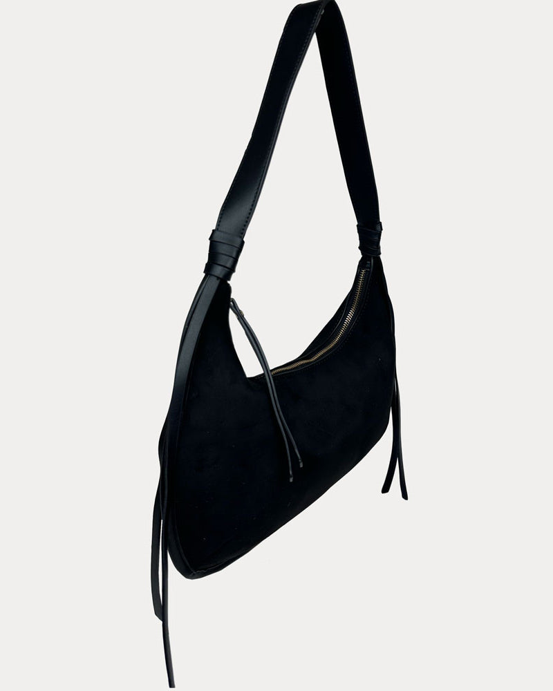 A black vegan suede shoulder bag with a vegan leather strap and hanging tassels, shown against a light gray background.