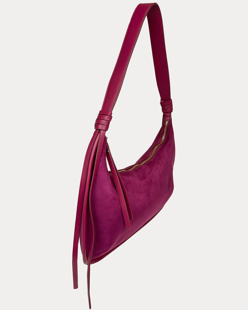 A burgundy vegan suede shoulder bag with vegan leather strap and tassel detail, shown from a side profile view against a light gray background.