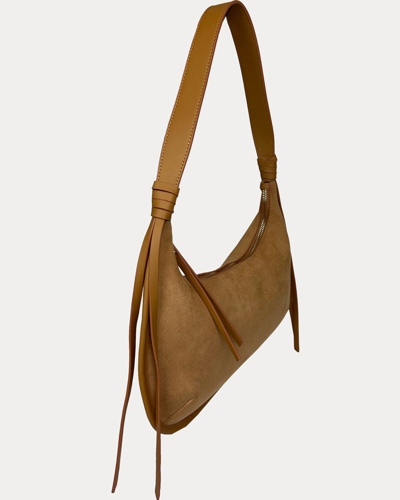 A camel vegan suede shoulder bag with a vegan leather strap and hanging fringe details, shown from a side profile on a light gray background.