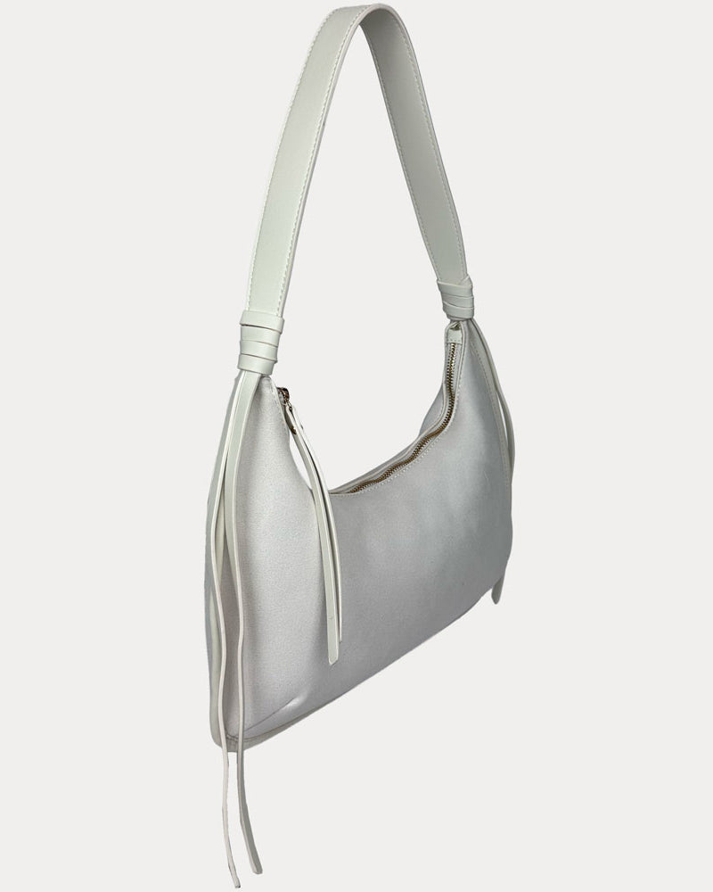 A cream vegan suede shoulder bag with a vegan leather strap and tassel details, shown from a side profile view against a light gray background.