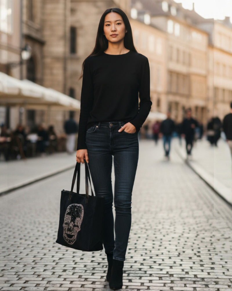 Woman in black outfit holding a black tote bag with a face design on a city street.