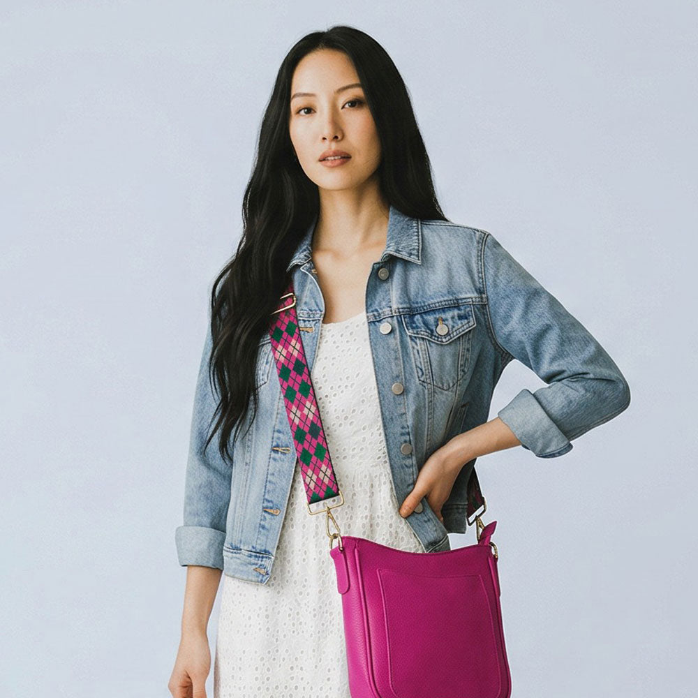 Woman wearing a denim jacket and wearing a pink bag with a argyle pattern bag strap against a light gray background
