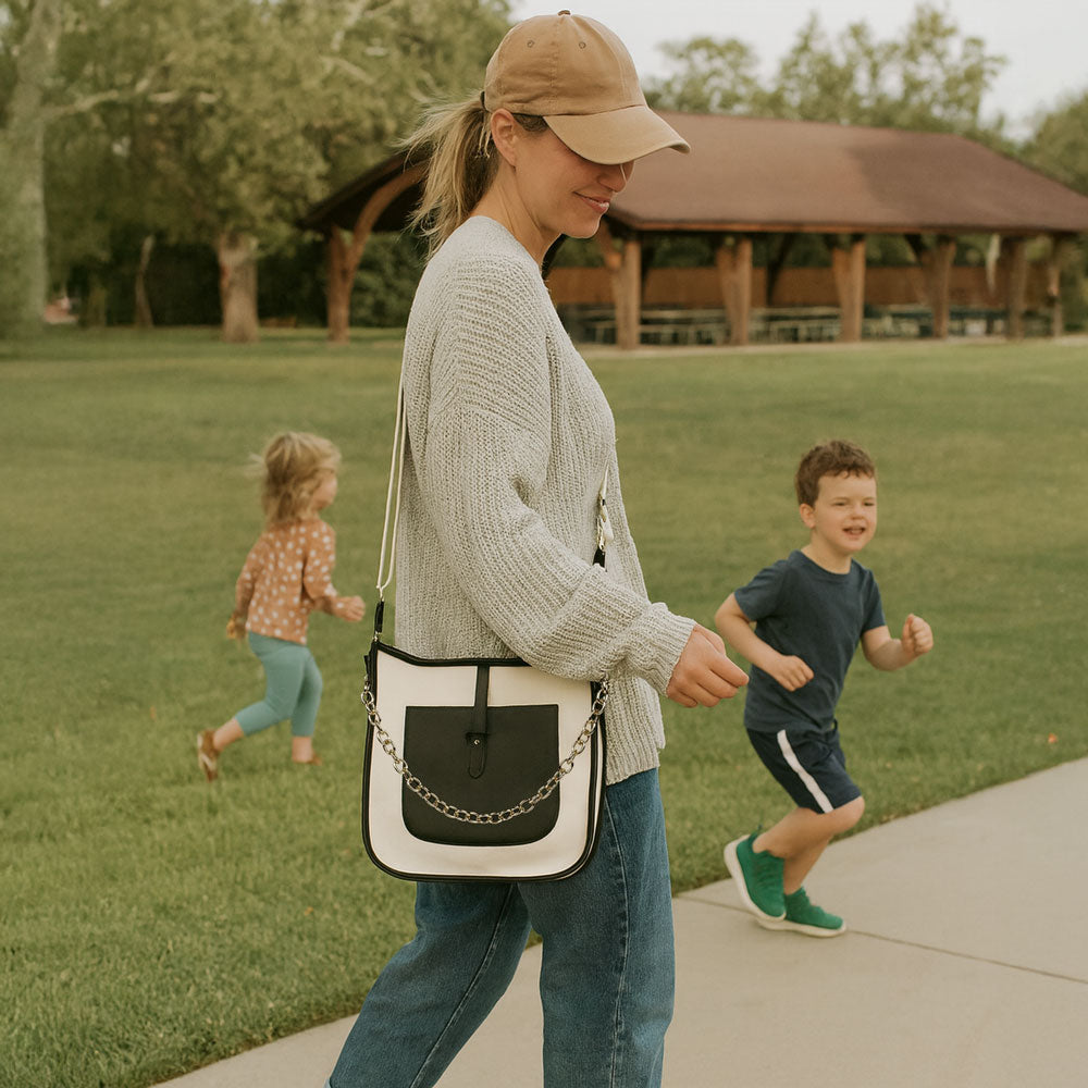 Woman walking with two children in a park, carrying a cream and black canvas handbag.