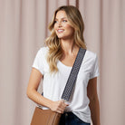 Woman wearing a brown handbag with a navy, tan, and blue zig zag pattern strap with gold hardware against a beige background