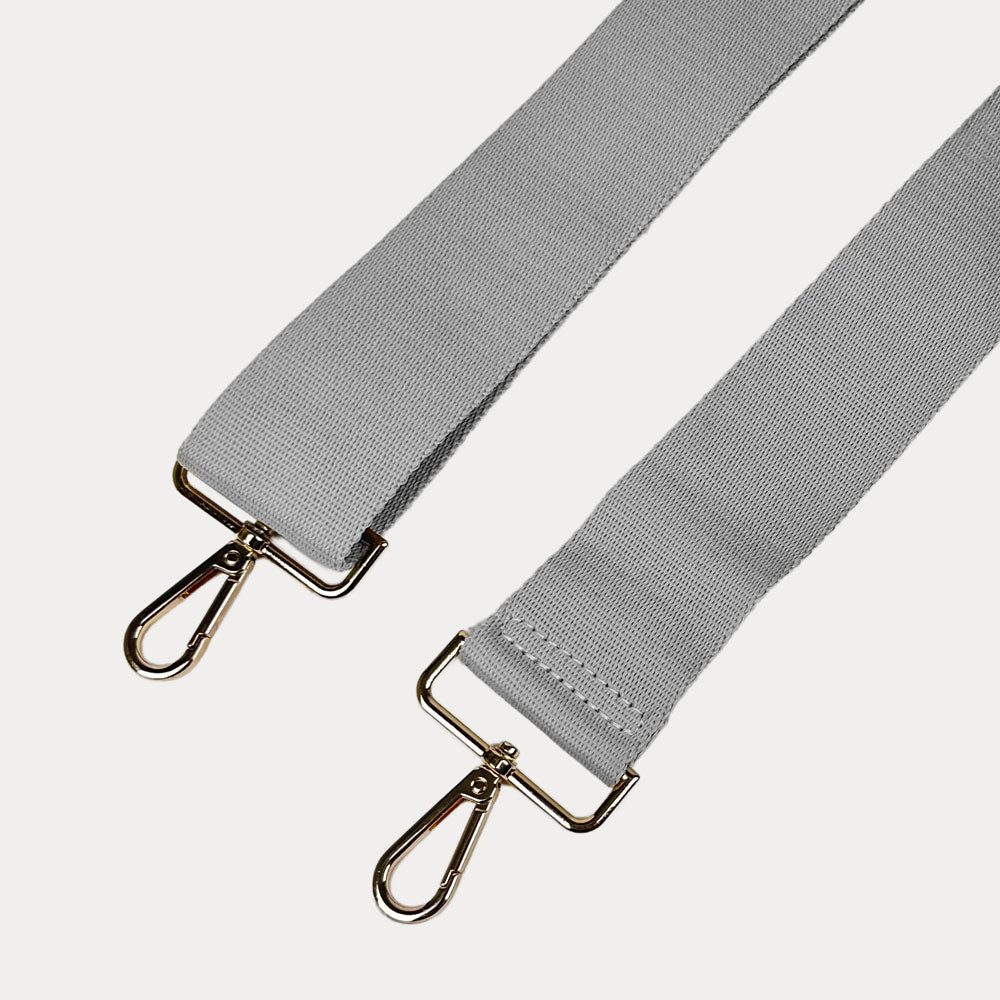 Gray bag strap with gold hardware on a light gray background