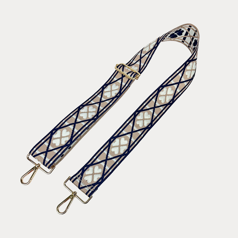 Tan, white, navy patterned bag strap with gold metal clasps on a light grey background.