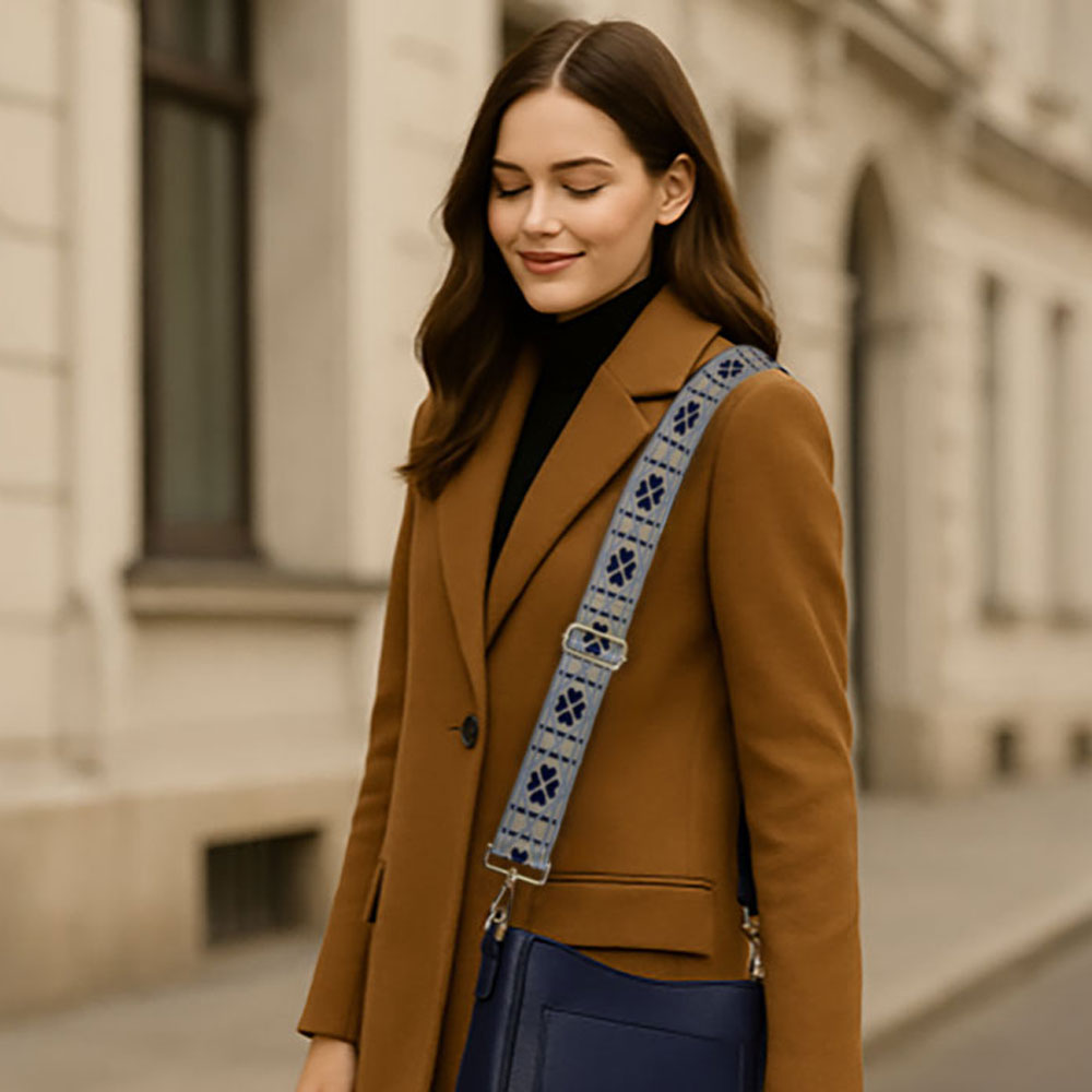 Woman in a brown coat with a patterned bag strap and navy crossbody bag walking on a street.