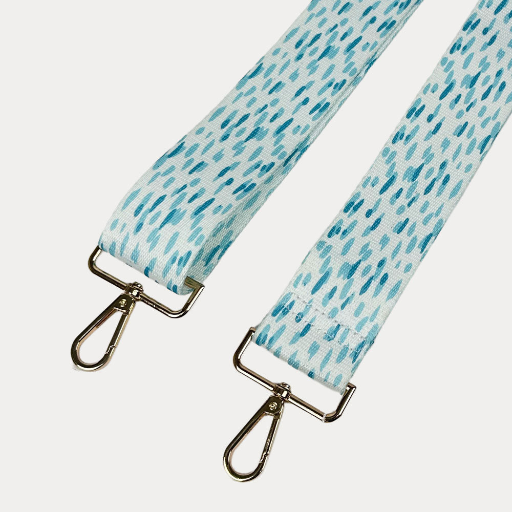 Aqua and white dot patterned bag strap with gold hardware on a light gray background