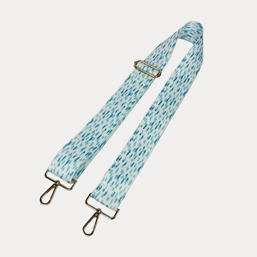 Aqua and white dot patterned bag strap with gold hardware on a light gray background